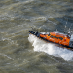 An orange RNLI boat speeding across the sea